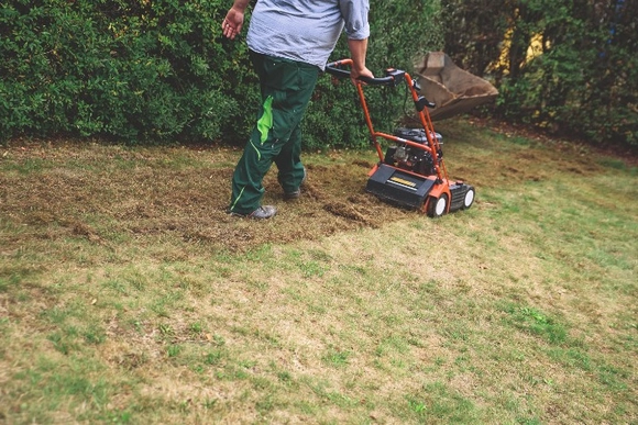 Person vertikutiert Rasen